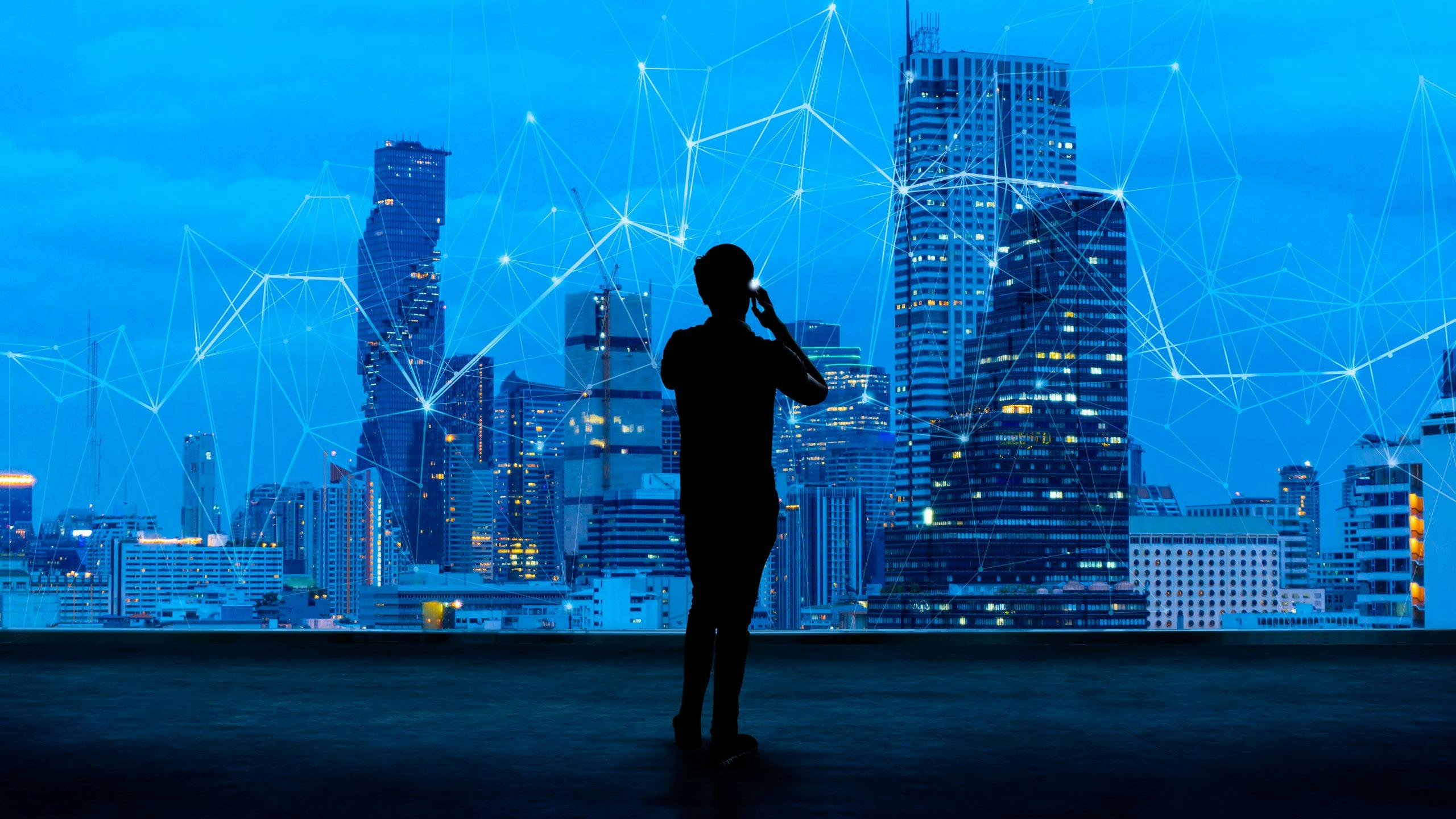 Building an agile digital workplace for an AI world - showing silhouette of a business man on mobile overlooking a network overlayed across a skyline