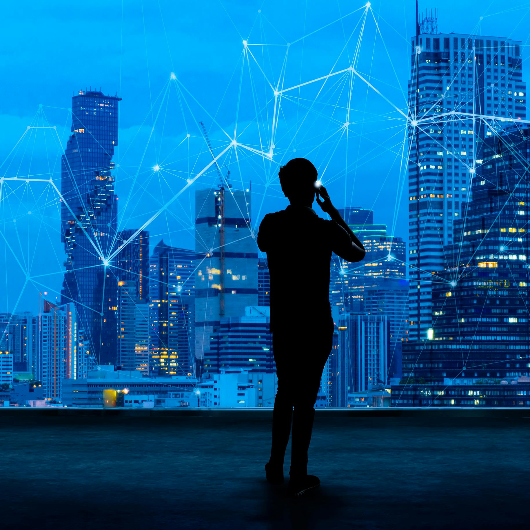 Building an agile digital workplace for an AI world - showing silhouette of a business man on mobile overlooking a network overlayed across a skyline