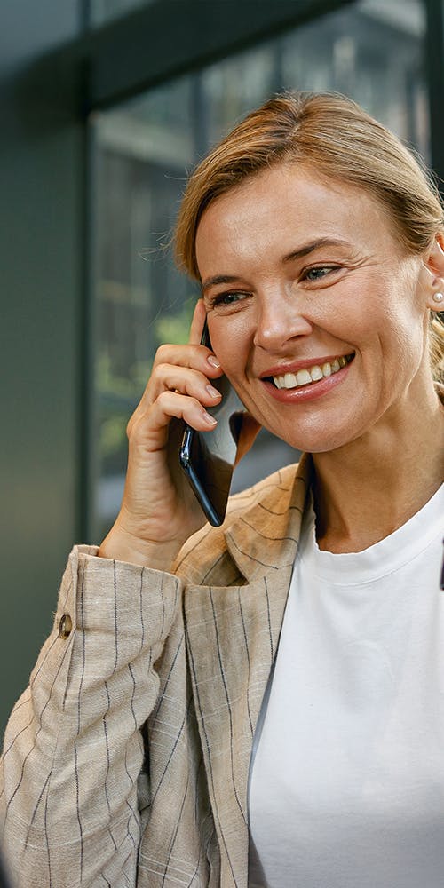 Woman on a business call on mobile phone looking at laptop holding a coffee