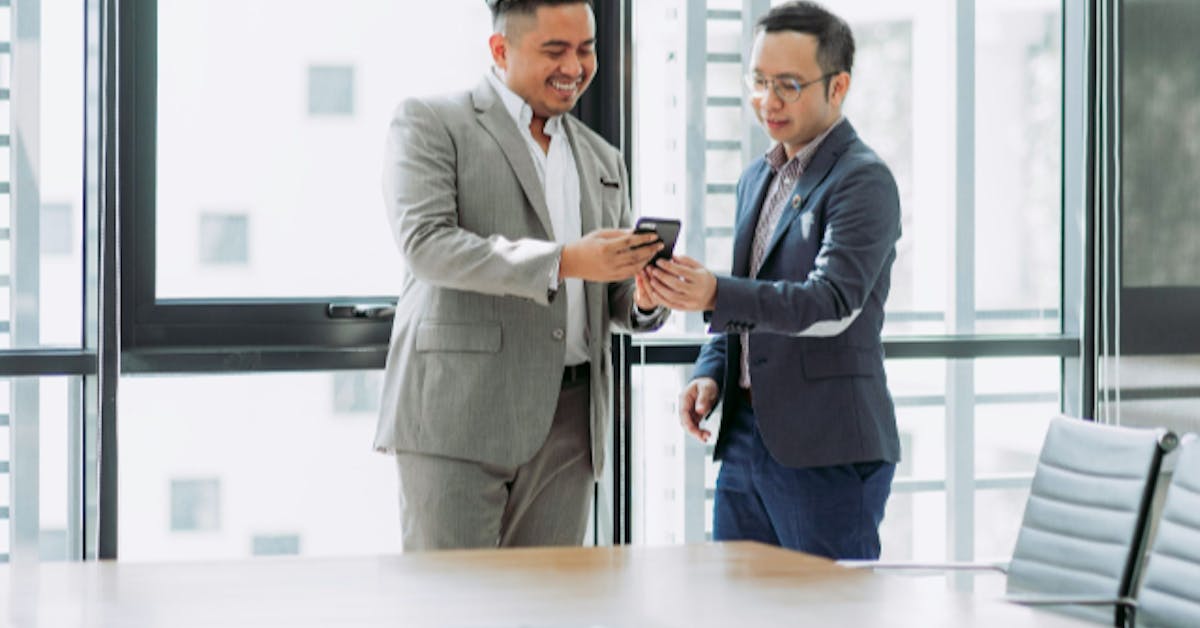 Two happy business men sharing message on phone in a bright office