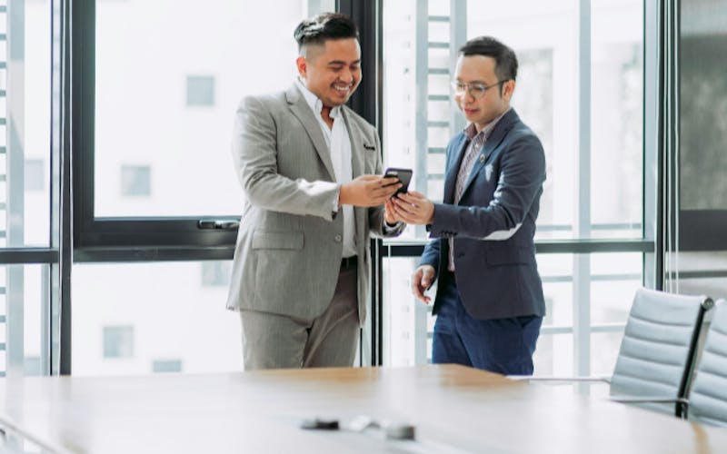 Two happy business men sharing message on phone in a bright office