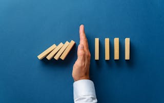 VOSS blog - How to manage and mitigate the impact of UC downtime. Image shows a hand stopping dominos in a conceptual image of business crisis management.