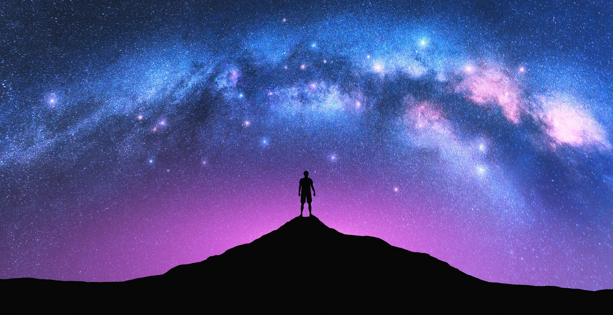 Milky Way arch and man on the mountain peak at starry night. Silhouette of alone guy, pink sky with bright stars