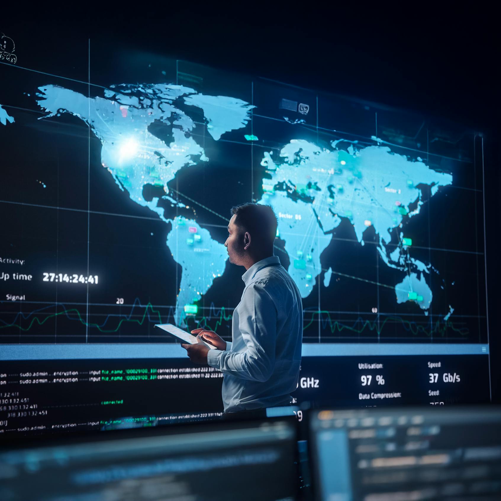 Security by design blog: Project Manager Walks to a Big Screen with Global Map. He is Using a Tablet. Team of Professional Computer Data Science Engineers Work in a System Control and Monitoring Telecommunications Office