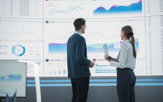 Business man and woman discussing UC analytics in front of a large screen full of statistics