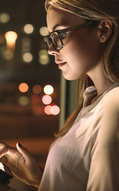 Sideways view of a woman wearing glasses reading a tablet in the dark