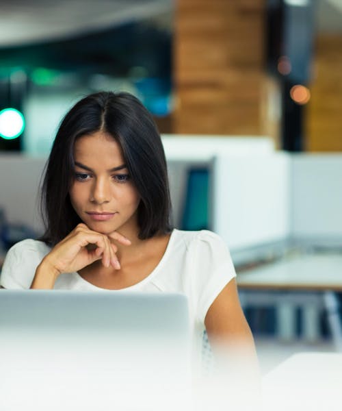 Young business woman working on laptop with hand under chin