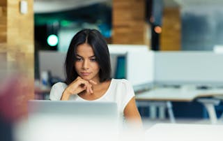 Young business woman working on laptop with hand under chin