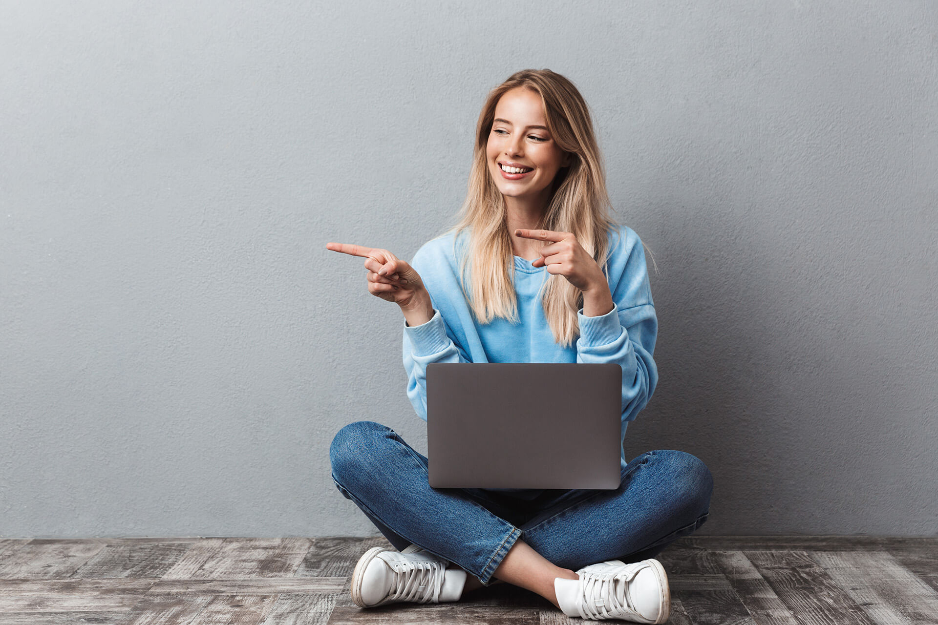 Simplify your UC workplace management with VOSS - young woman sitting on floor with laptop pointing to the right