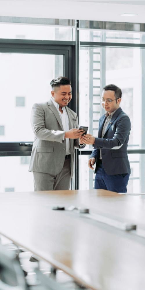 Two happy business men sharing message on phone in a bright office