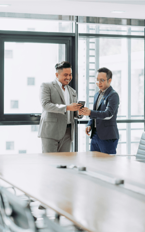 Two happy business men sharing message on phone in a bright office